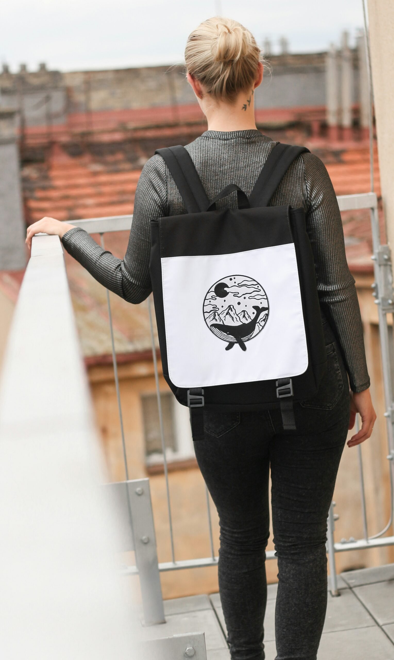 selective focus photography of woman wearing black and white backpack standing on terrace while holding handrails